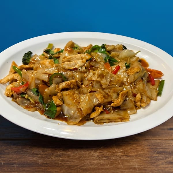 A white plate of Pad See Ew with chicken, wide noodles, broccoli, and red peppers.