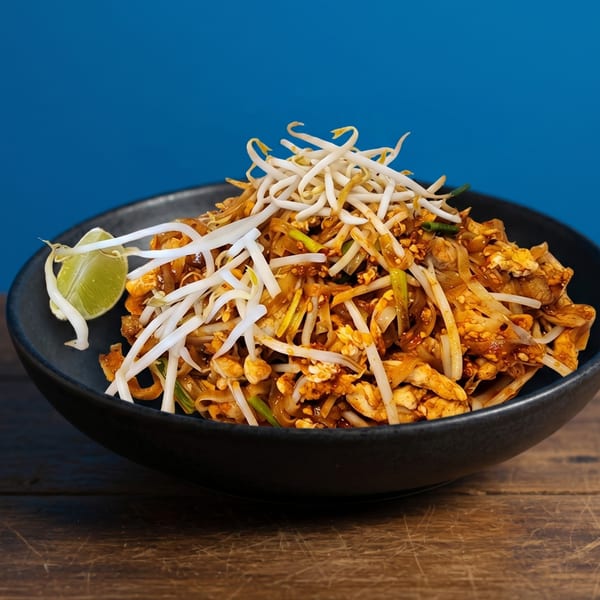 Pad Thai noodles with chicken, bean sprouts, and a lime wedge in a black bowl.