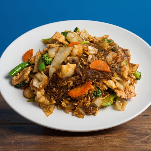 Glass noodles with chicken, broccoli, carrots, snap peas, and cabbage on a white plate.